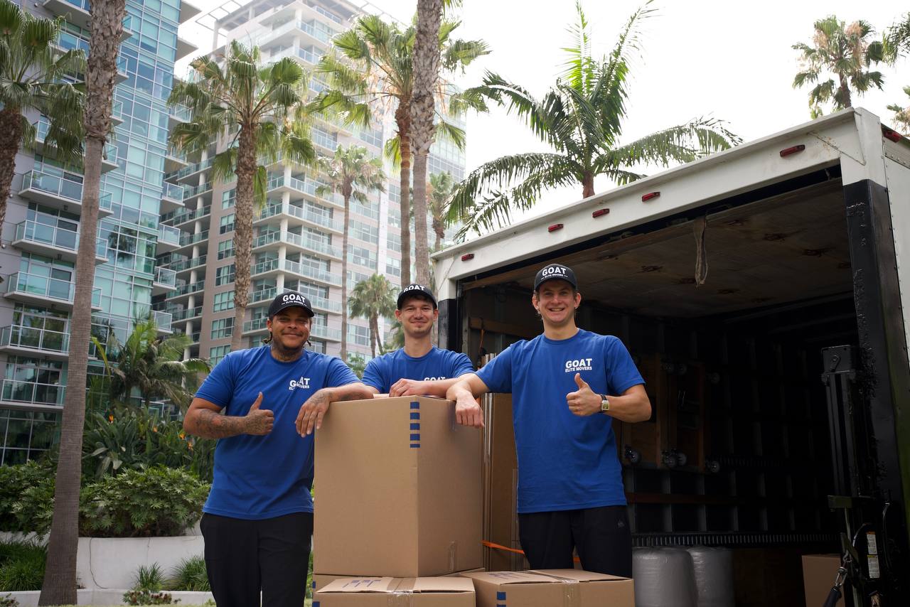 Three GOAT movers smiling with boxes by the truck