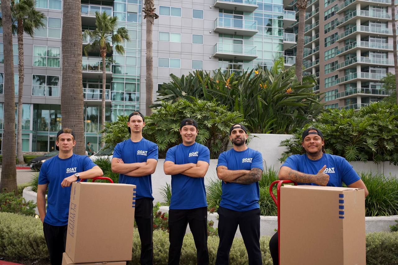 GOAT Elite Movers crew posing with boxes in front of a Los Angeles high-rise