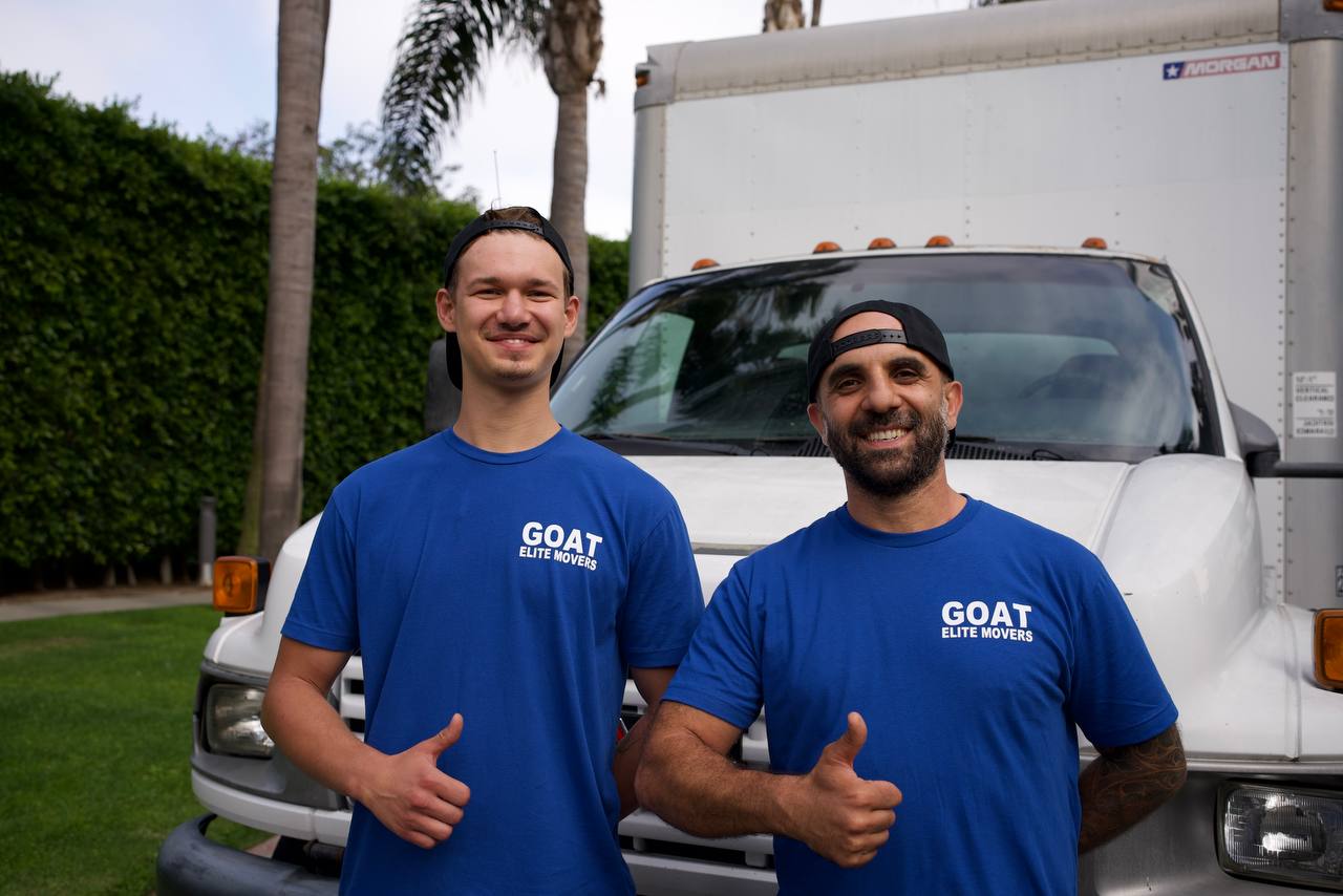 Two friendly GOAT movers giving thumbs up in front of the moving truck
